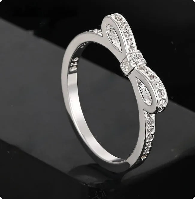 A silver-coloured bow-shaped ring set with sparkling clear rhinestone crystals on a finger.