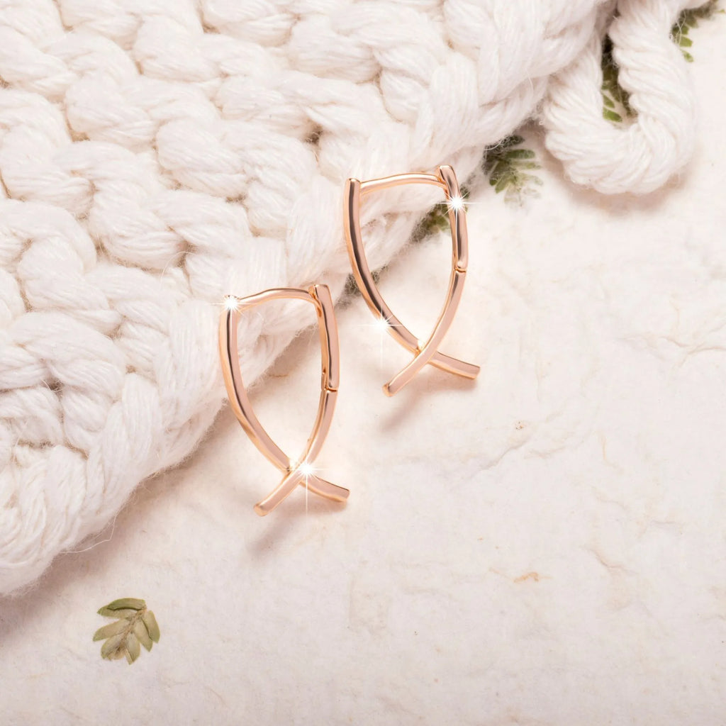 Rose gold cross shaped fashion earrings made from copper on a white background