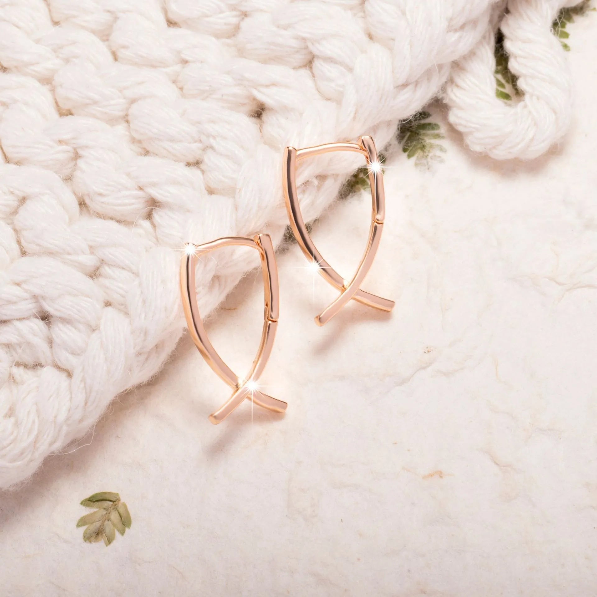 Rose gold cross shaped fashion earrings made from copper on a white background