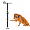 Silver metal dog training bells on an adjustable black nylon leash hanging from a door handle.