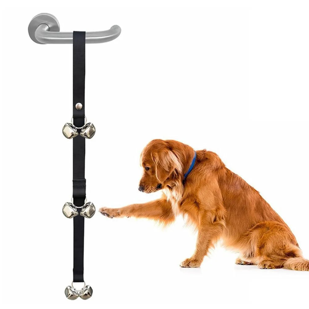 Silver metal dog training bells on an adjustable black nylon leash hanging from a door handle.