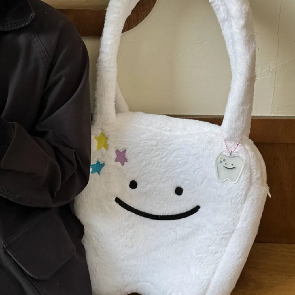 White plush tote bag with large cute teeth graphic, showing crossbody strap and zip opening.