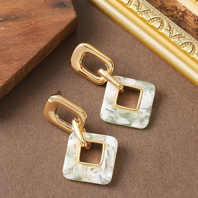 A pair of hollow geometric square earrings with a chamfered pattern, shown in an electroplated finish.