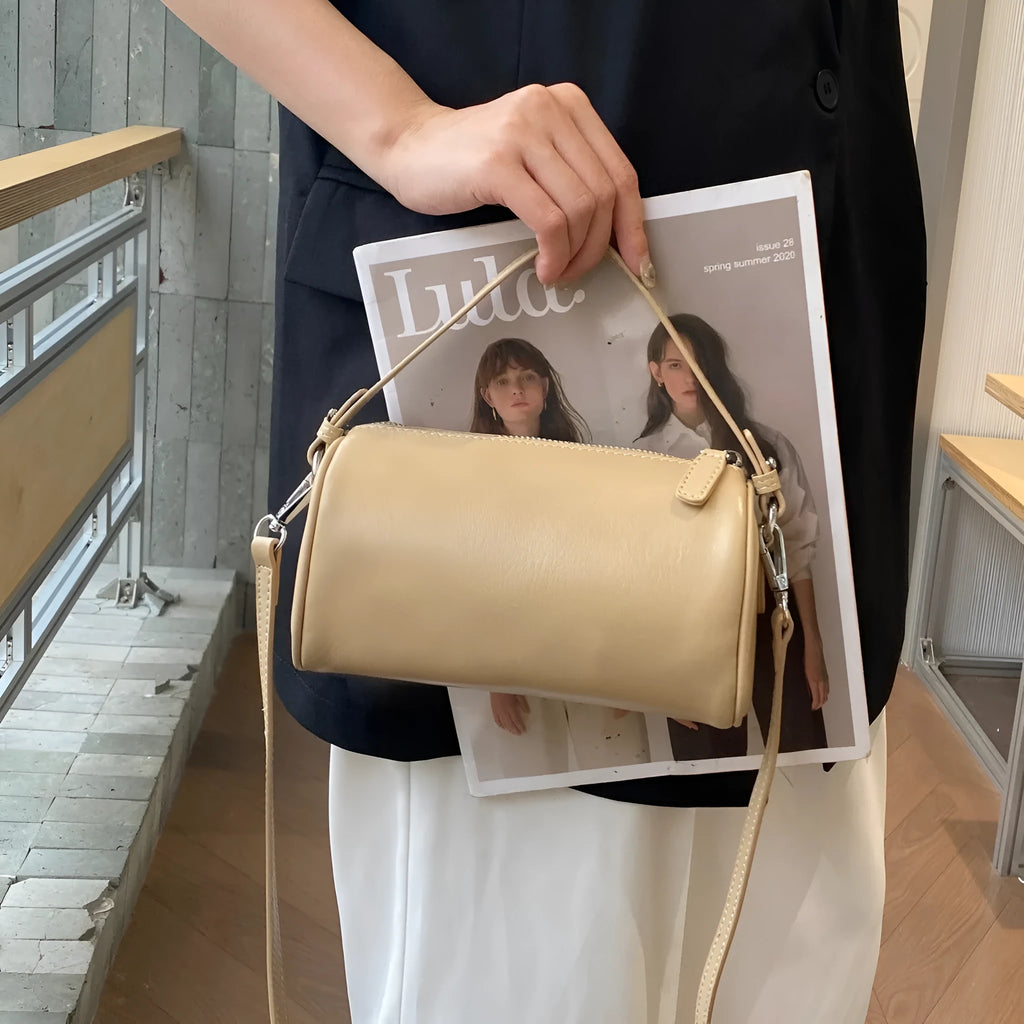 Brown cylindrical leather crossbody phone bag with visible stitching on a flat surface.
