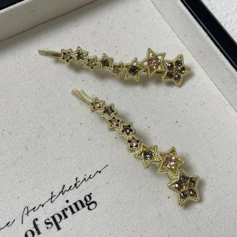 Gold-coloured alloy hair barrette with a side clip, rhinestones, a star, and a word decoration.