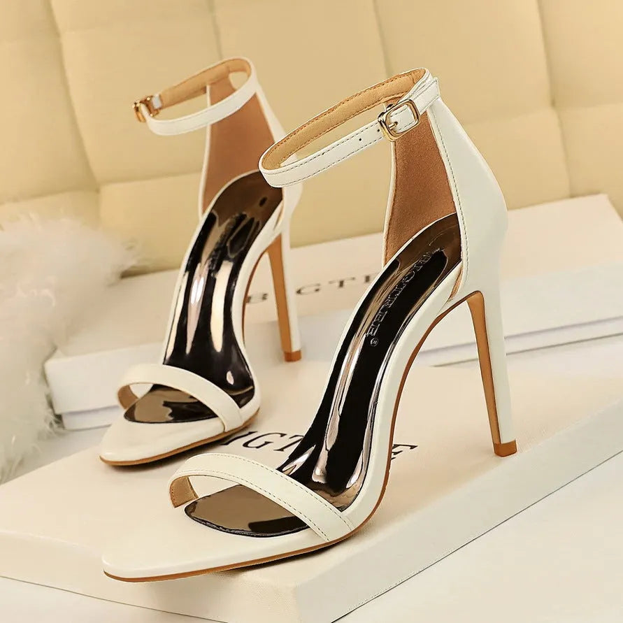 White open-toe high-heel sandals with an ankle-strap buckle on a woman's foot.