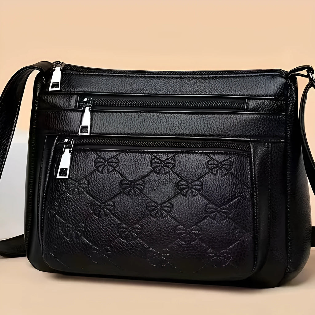 Black women's crossbody bag with butterfly embossed pattern and adjustable shoulder strap.
