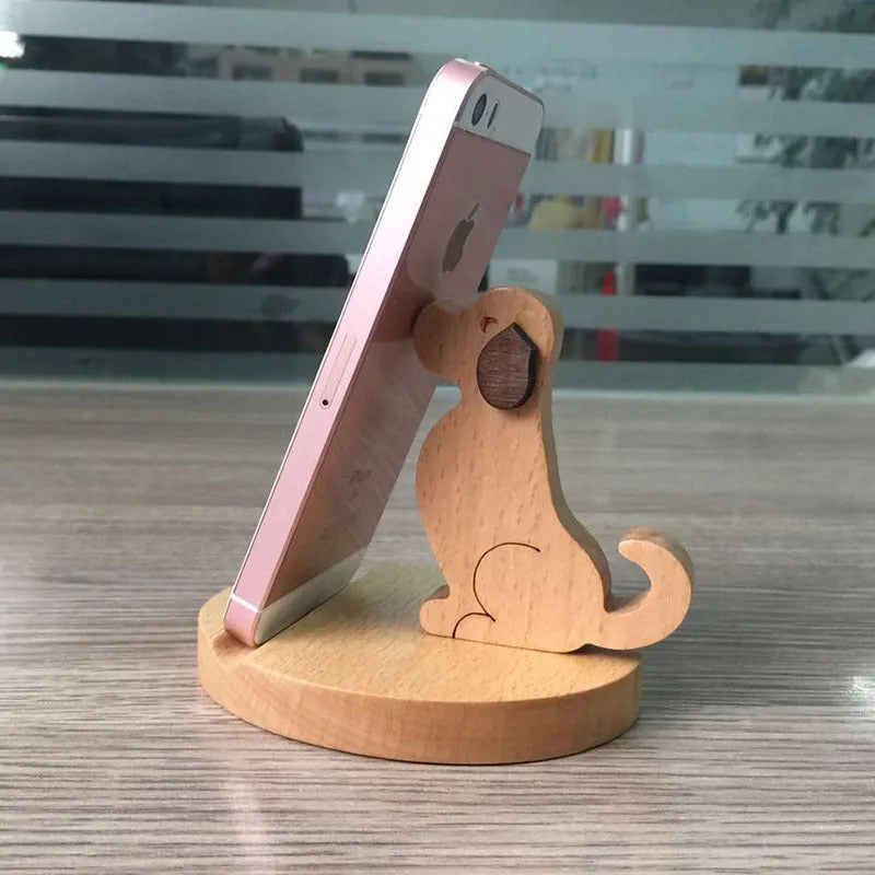 Solid wood cartoon puppy phone bracket with brown spray paint on a desk holding a smartphone upright.
