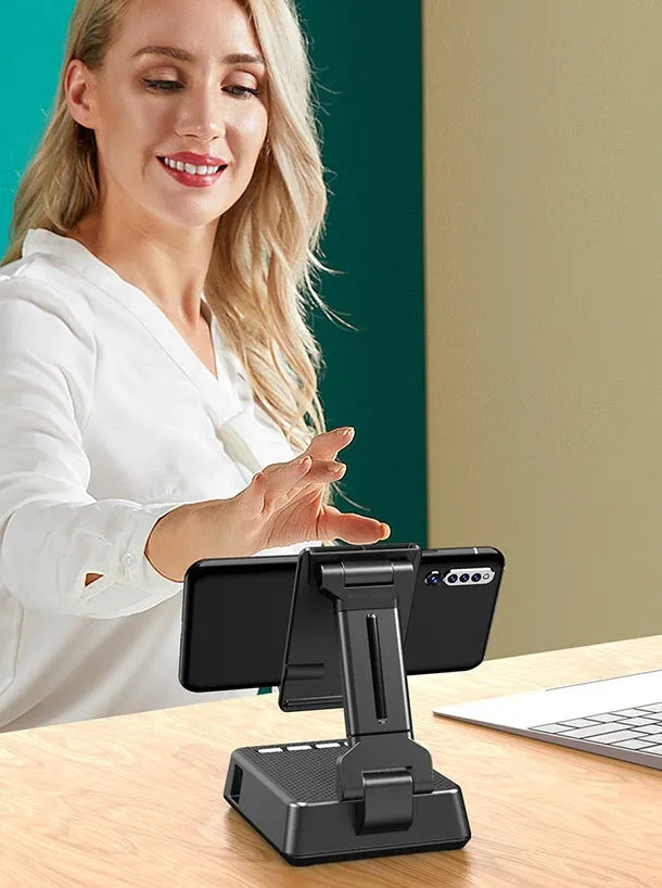 Black mobile phone broadcasting stand with integrated Bluetooth speaker on a desk.