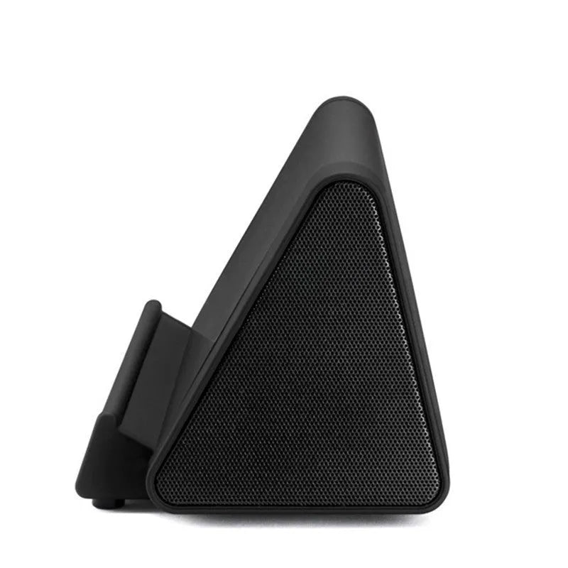 Small black or white wireless Bluetooth speaker with built-in charging cable on a desk next to a mobile phone