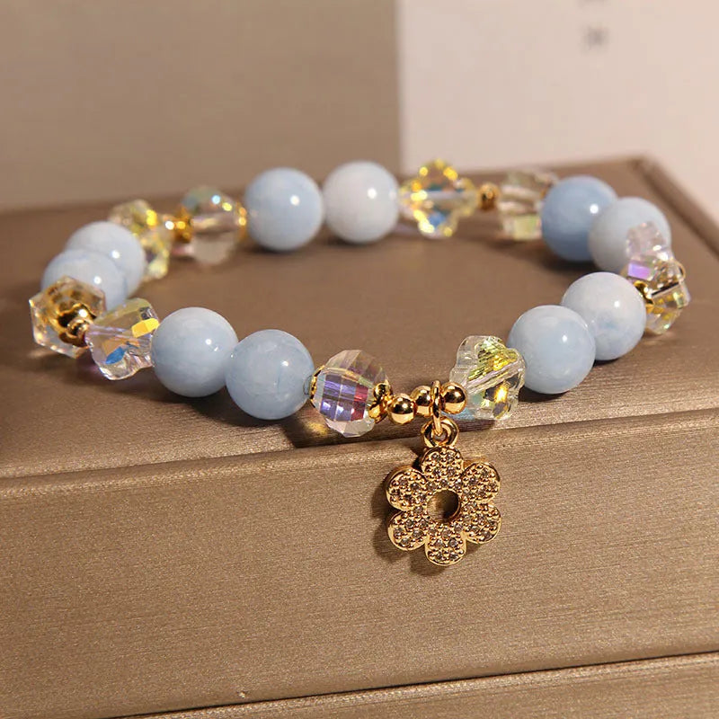 Women's aquamarine crystal bracelet with four-leaf clover charm and pearl details on a wrist.