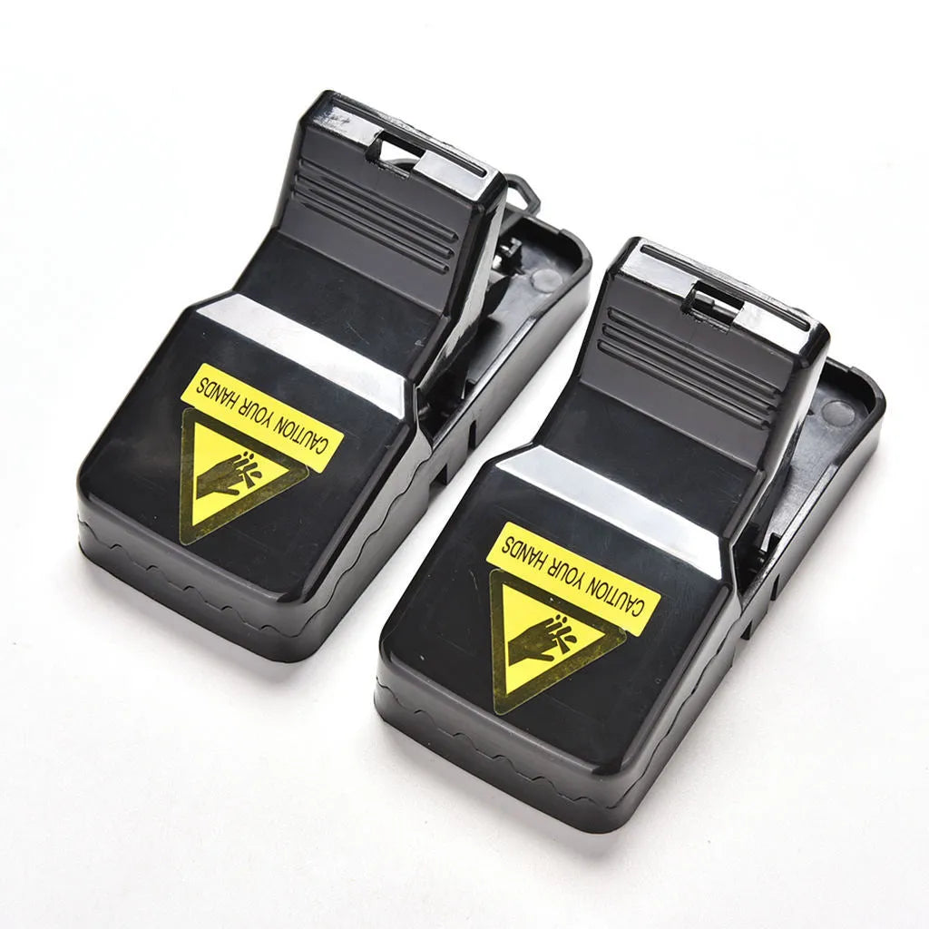 Set of six black plastic snapping mousetraps with smooth surfaces, shown next to a ruler for scale.