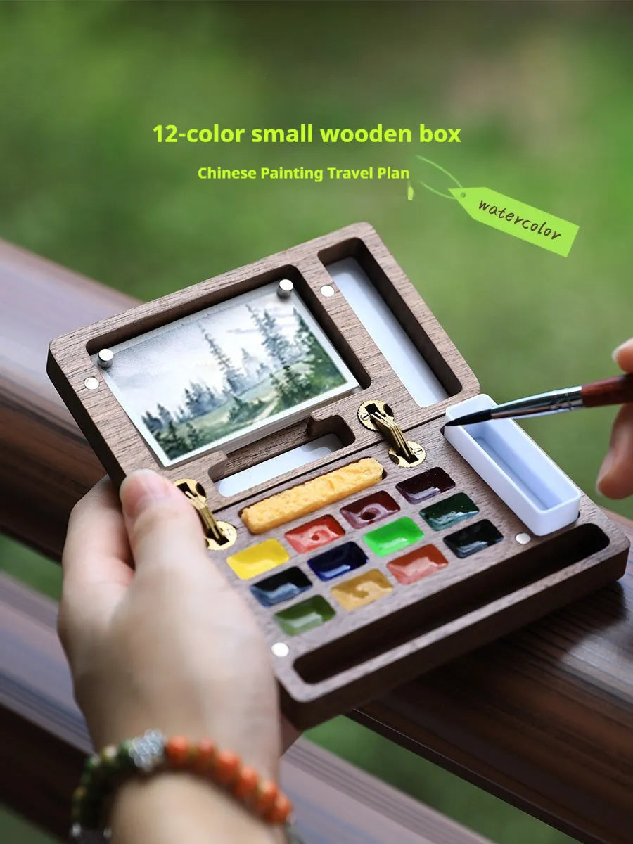 Small wooden watercolour paint box open to show artist pigment pans inside for portable painting.