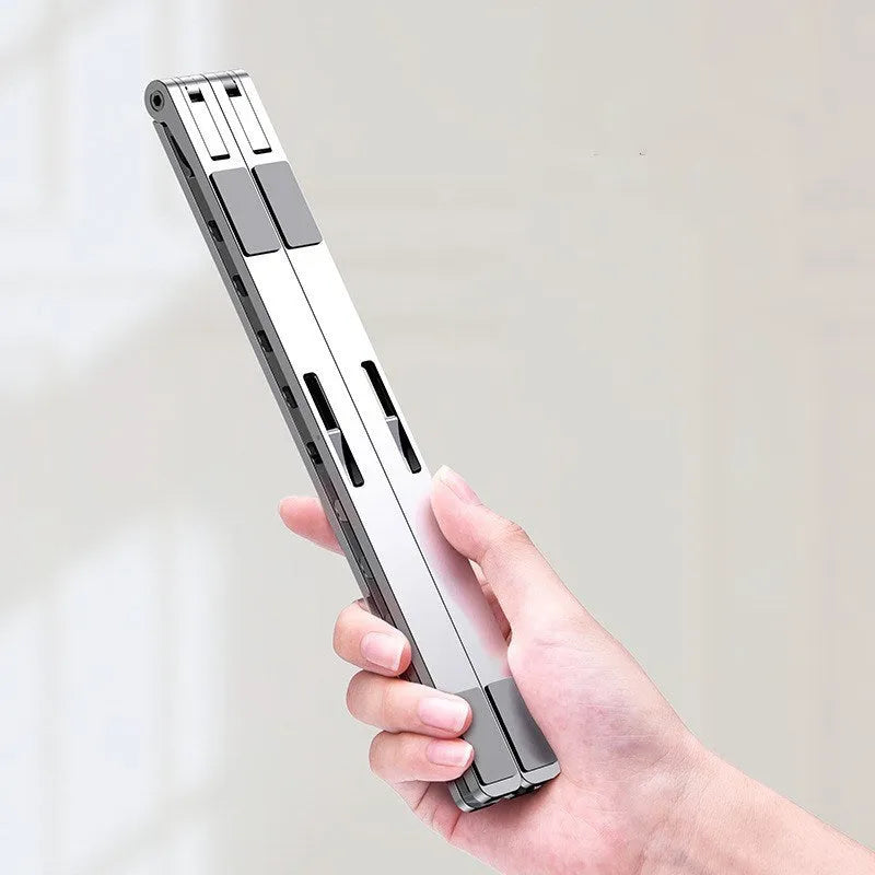 Grey folding aluminium alloy laptop bracket with silicone grip on a desk, angled to hold a notebook