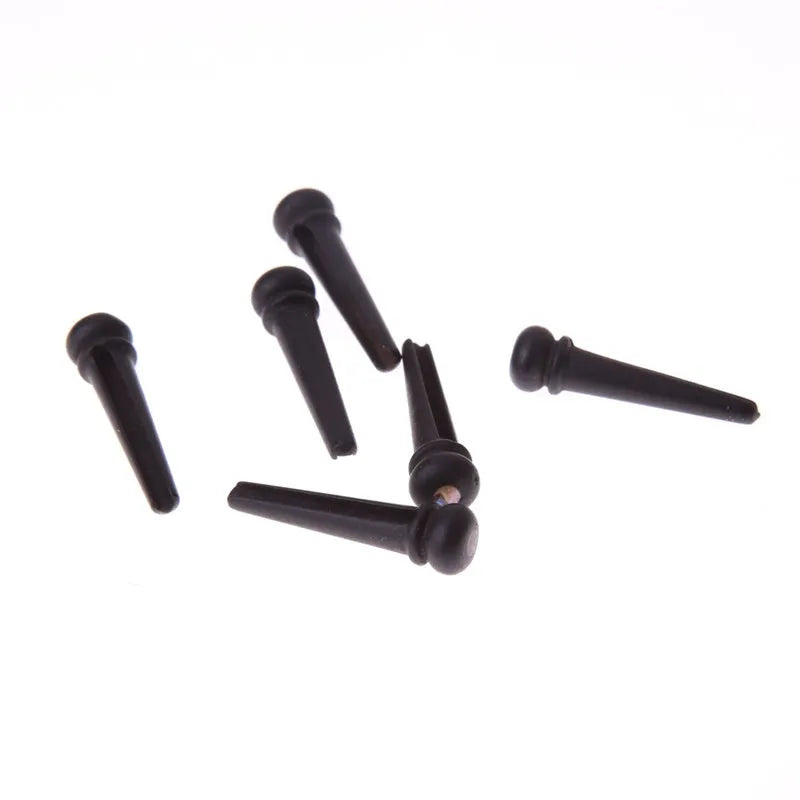 Six matt black ebony guitar string nails for folk acoustic guitars on a white background.