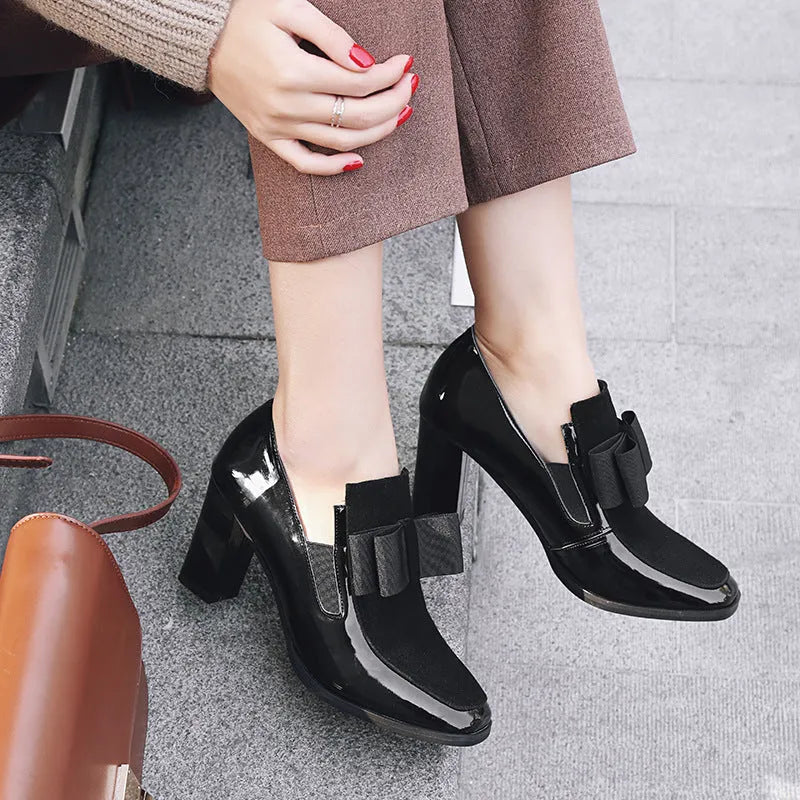Black patent leather high heels with a thick block heel and square toe on a white background.