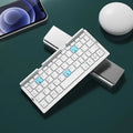 Aluminium folding Bluetooth keyboard with stand supporting smartphone, showing compact folded size