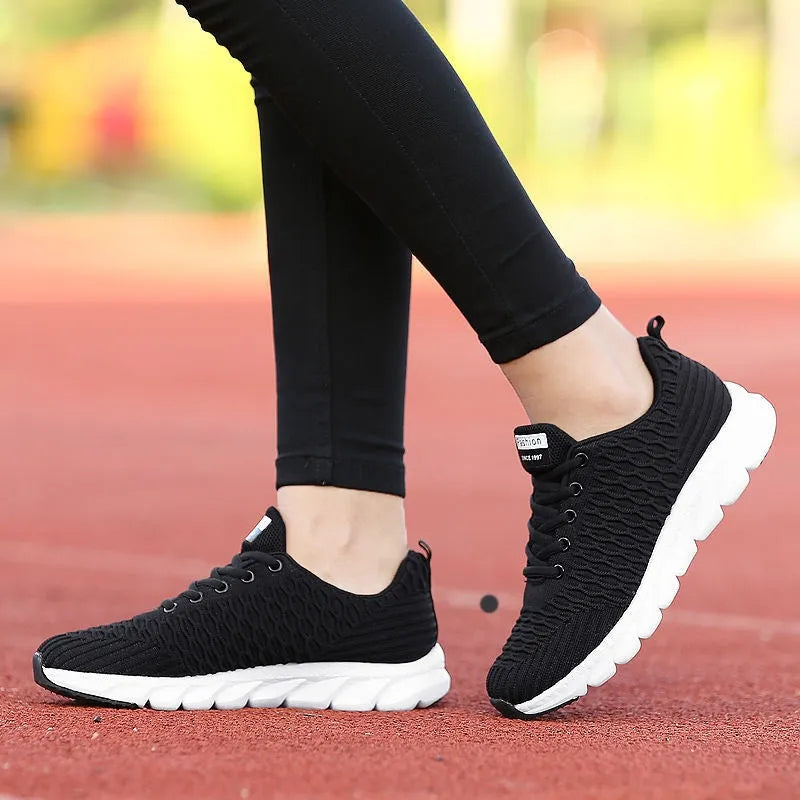 Women's black running shoes with a fly weave upper and a durable outsole on a track.