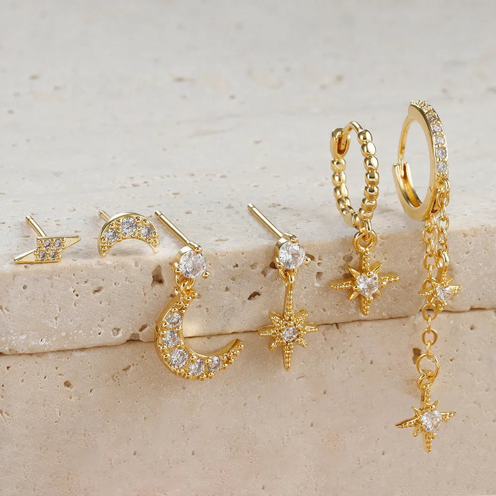 Set of six pairs of gold chain tassel drop earrings with zircon studs laid out on a surface.