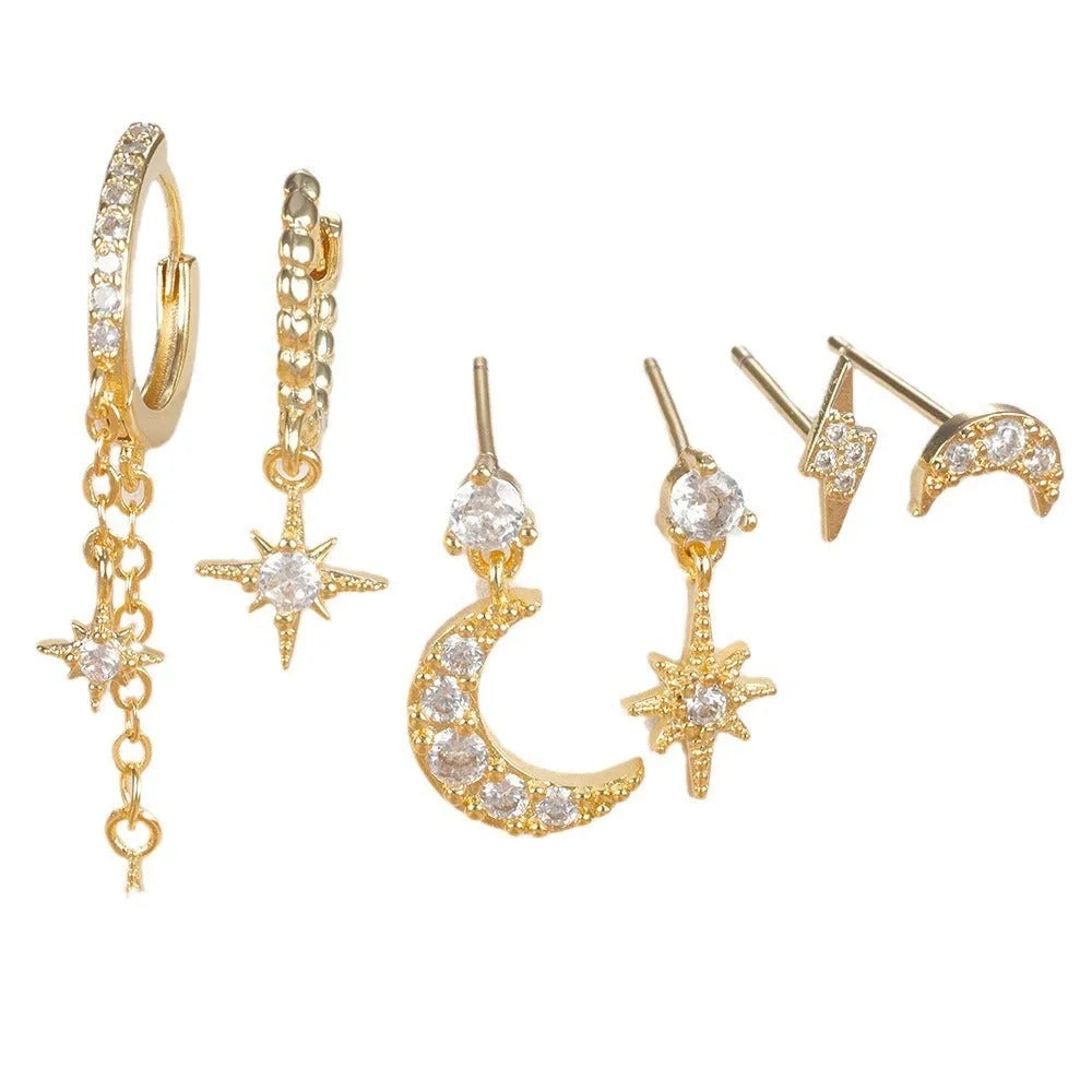 Set of six pairs of gold chain tassel drop earrings with zircon studs laid out on a surface.