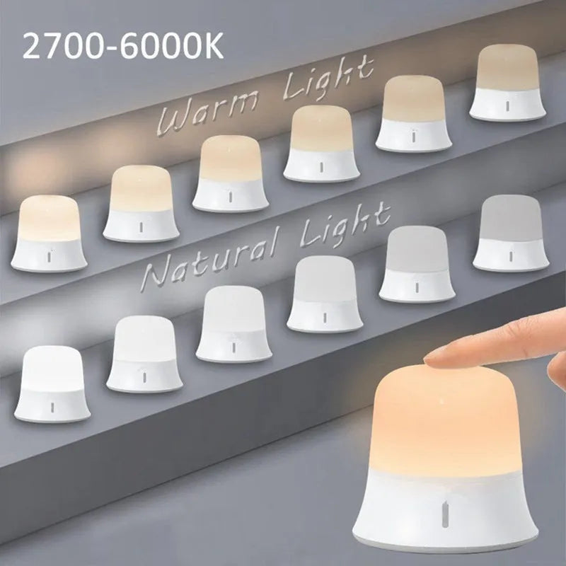 White cylindrical touch-control bedside night light with rechargeable battery on a table.