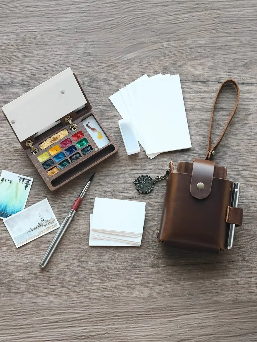 Small wooden watercolour paint box open to show artist pigment pans inside for portable painting.