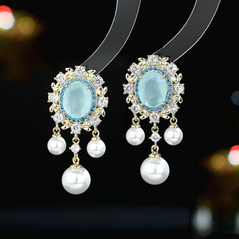 A pair of oval-shaped copper earrings with inlaid zircon stones and a dangling pearl tassel, shown in light purple.