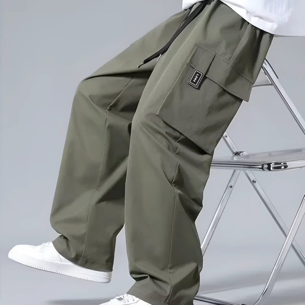 Boy wearing straight leg cargo pants with drawstring waist and large side pockets in army green.