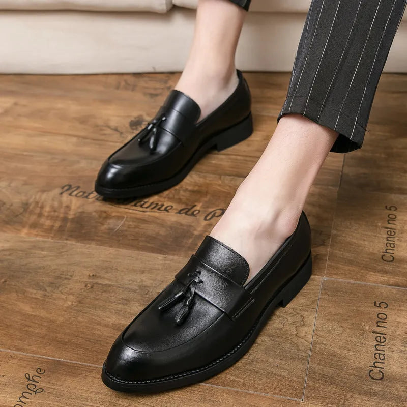 Men's black slip-on business casual shoes with tassel detail and plain toe on wooden floor