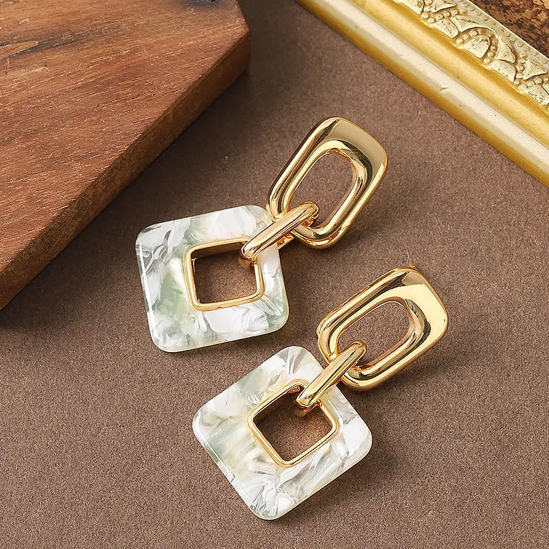 A pair of hollow geometric square earrings with a chamfered pattern, shown in an electroplated finish.