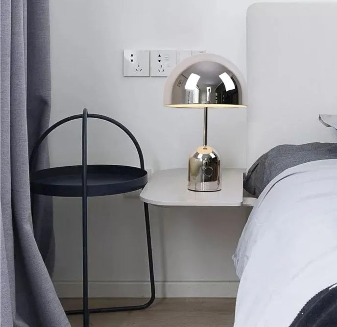 Modern mushroom cap table lamp with a metal base in rose gold finish on a wooden table.