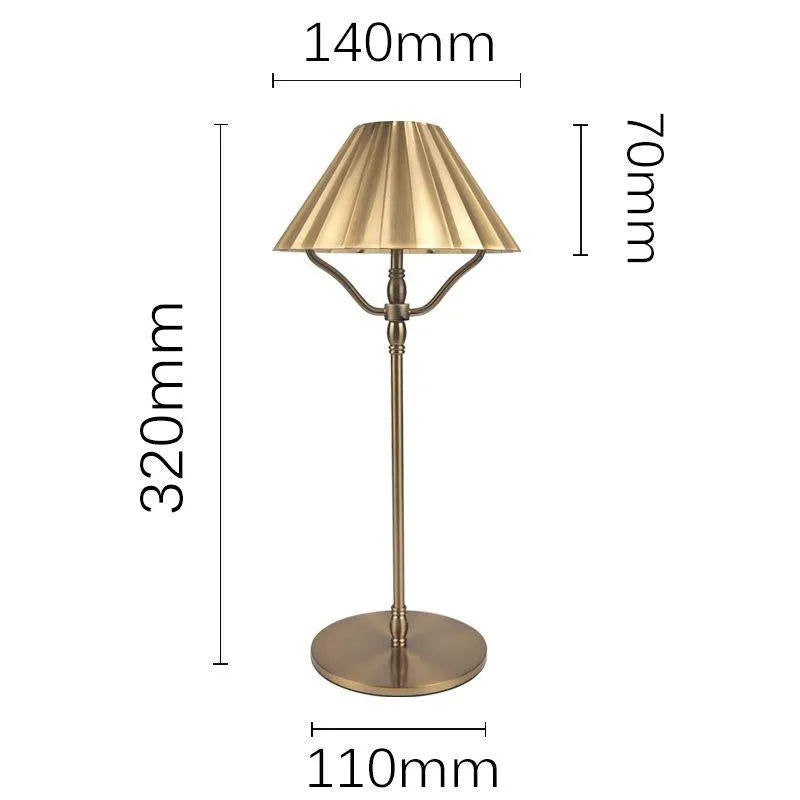 Gold-colour alloy desk lamp with a cylindrical shade on a wooden desk, showing a USB-C charging cable.