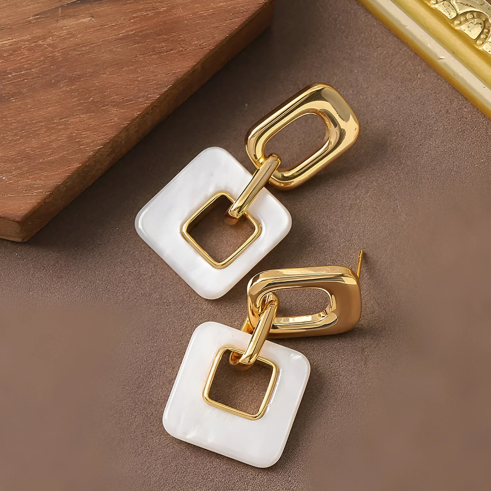 A pair of hollow geometric square earrings with a chamfered pattern, shown in an electroplated finish.