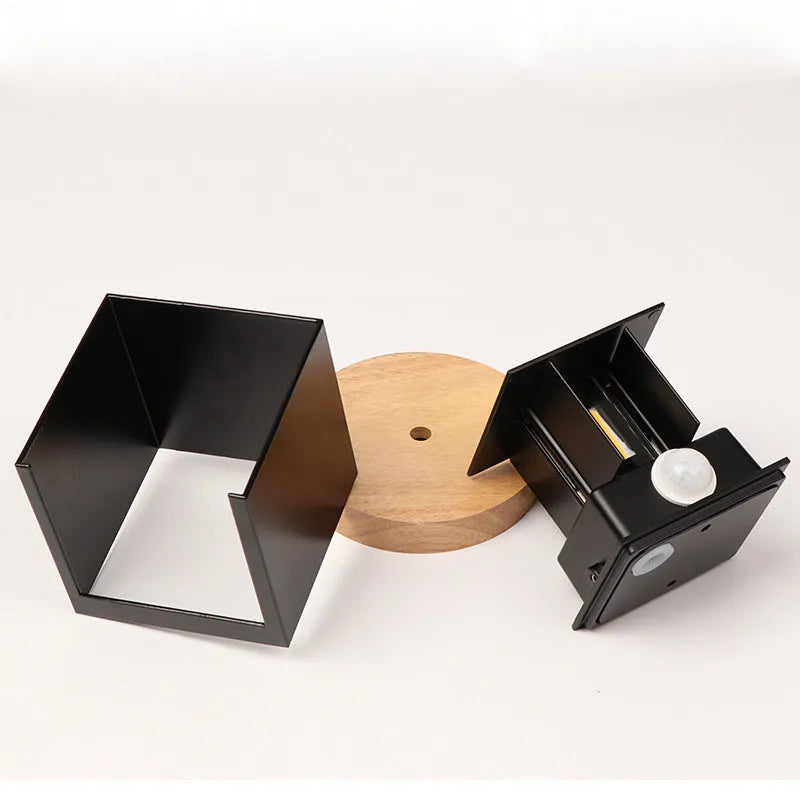 Square black aluminium alloy LED wall lamp mounted on a brick wall, showing 360-degree light emission.