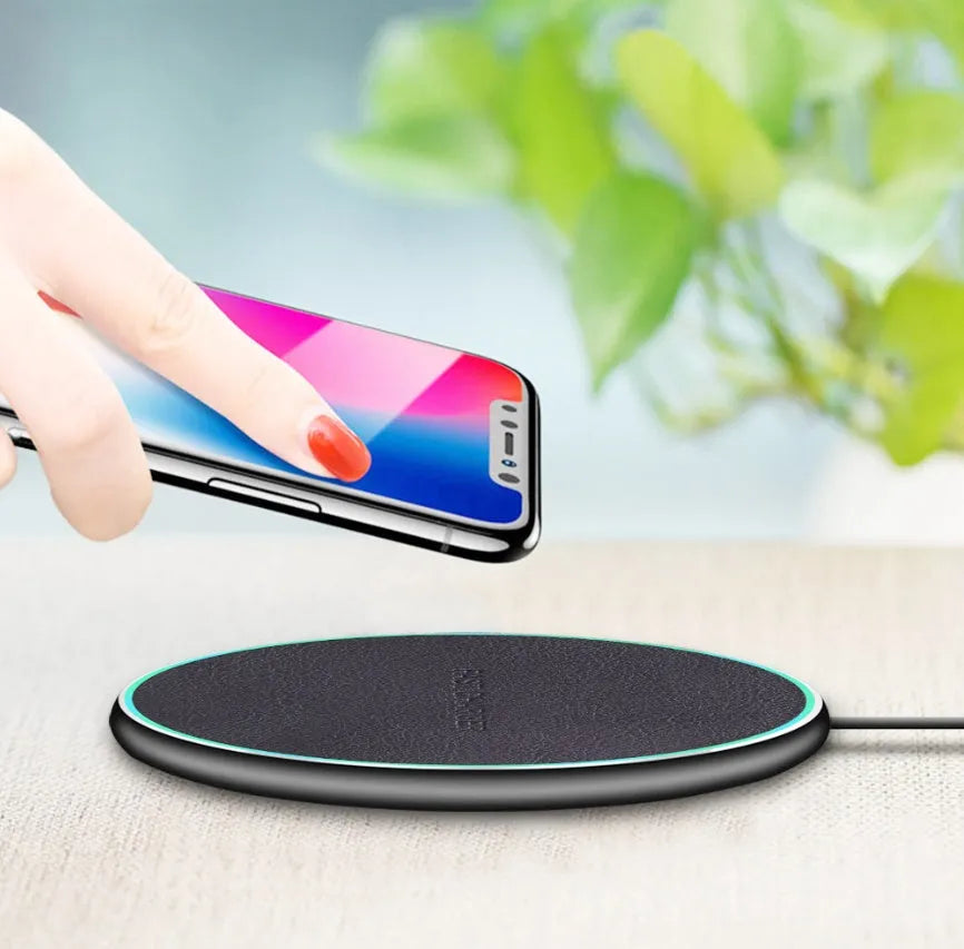 Black Qi wireless charging pad for iPhone 11 on a wooden surface.