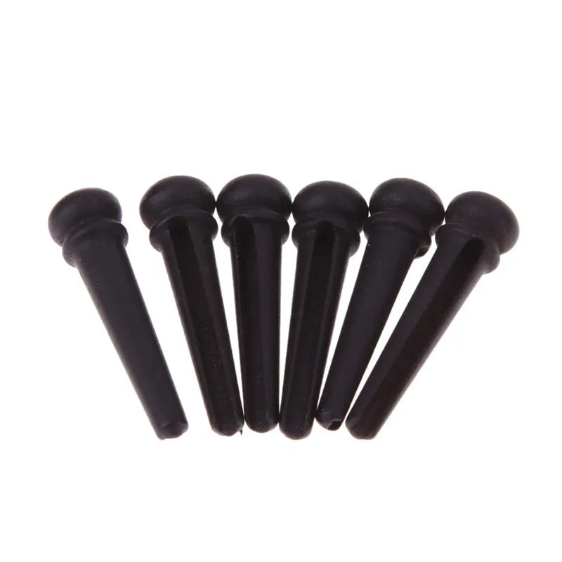 Six matt black ebony guitar string nails for folk acoustic guitars on a white background.