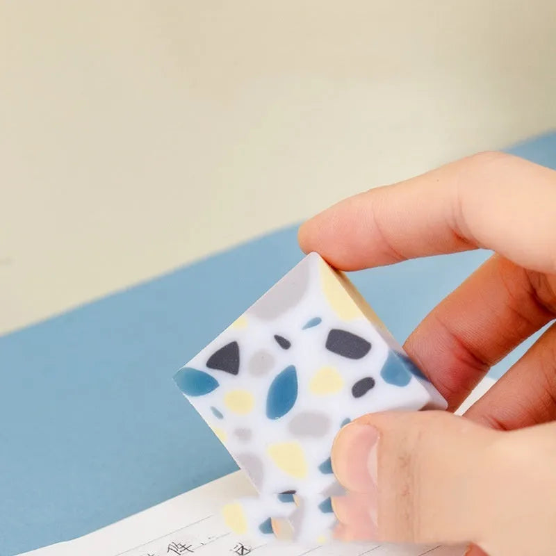 A single white rubber eraser in a brick shape with straight edges, for cleaning pencil marks from paper.