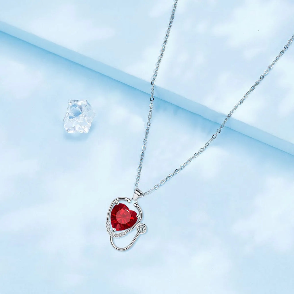 Red diamond women's necklace with a stethoscope, wings, and cross pendant on an adjustable chain.