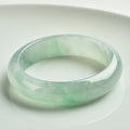 Light green jade bracelet on a white background, showing natural stone texture.
