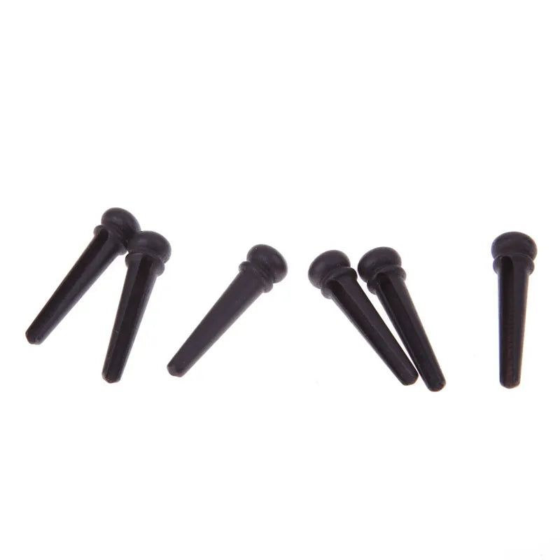 Six matt black ebony guitar string nails for folk acoustic guitars on a white background.