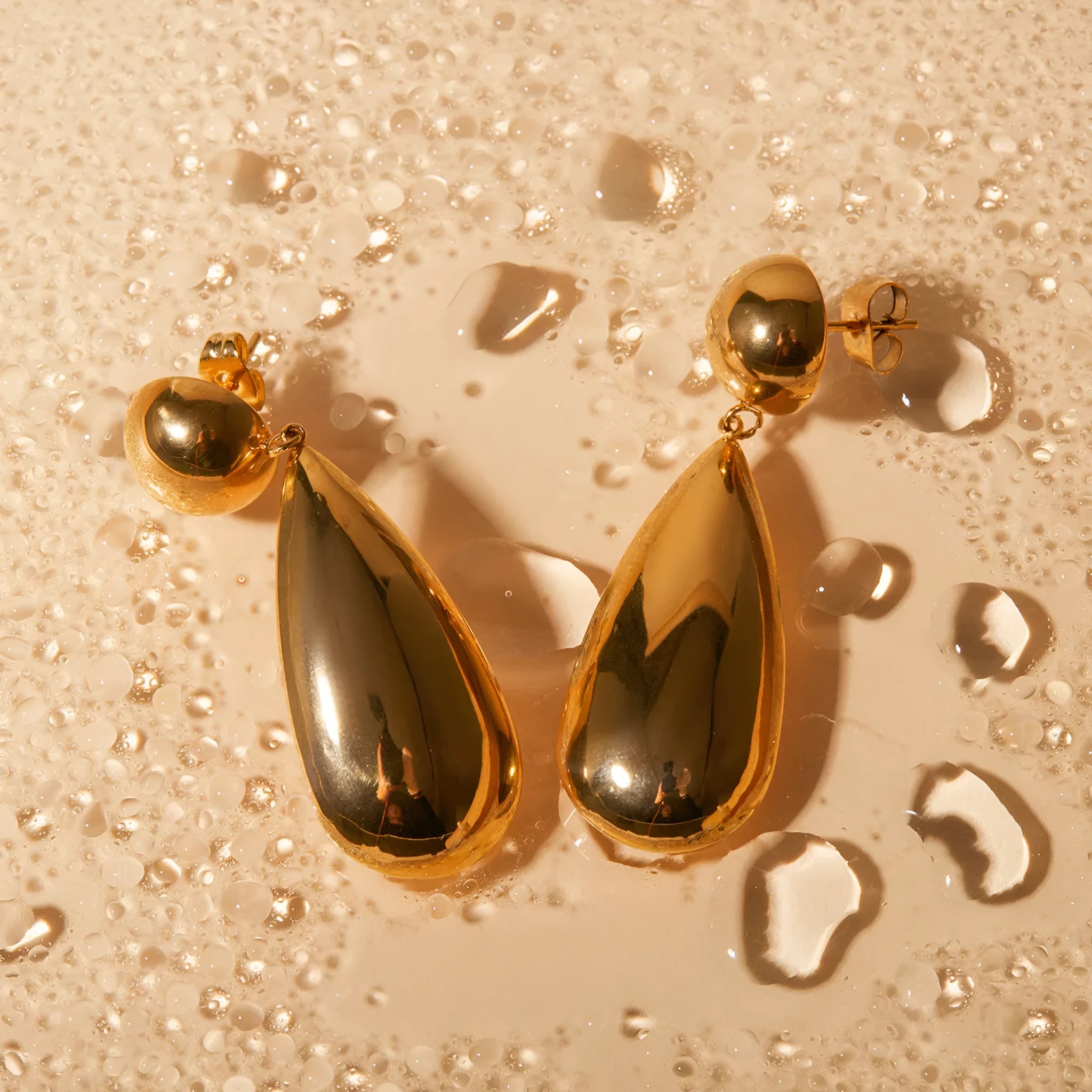 Gold electroplated stainless steel earrings with geometric hemisphere and water droplet pendant design