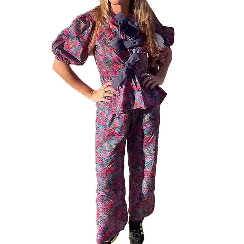 Women's floral print two-piece suit with a tie-neck puff sleeve blouse and straight-leg trousers.