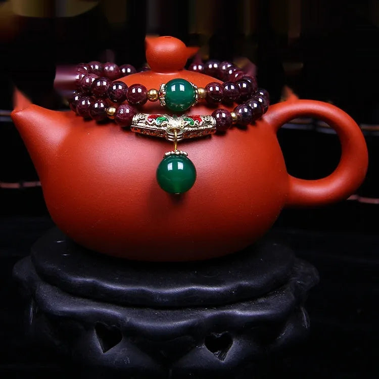 Natural deep red garnet bead bracelet with a golden toad charm, shown in 7mm size on a wrist.