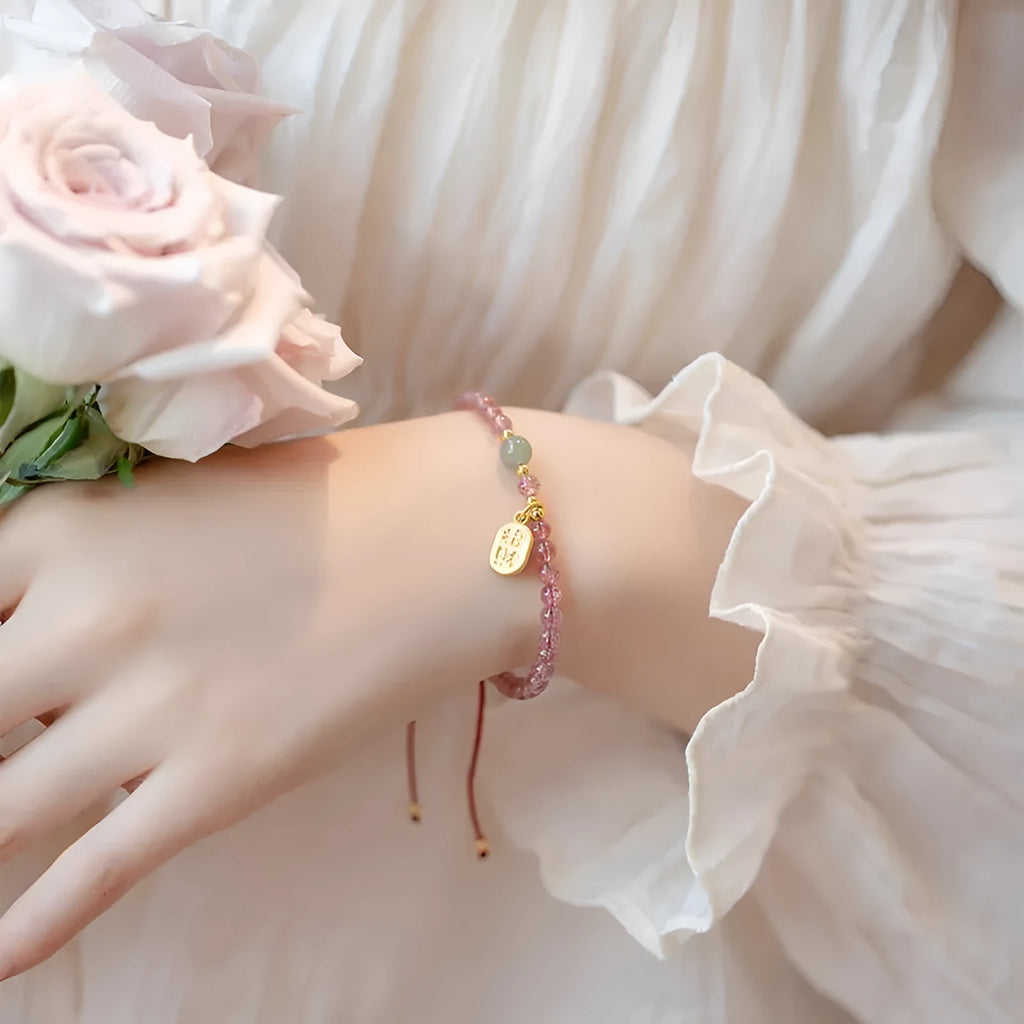 Hand-woven red rope bracelet with a strawberry quartz crystal charm on a wrist.