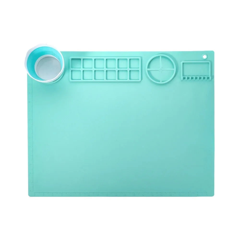 Light blue silicone painting mat with two bowl depressions for water and brushes, placed on a wooden table.