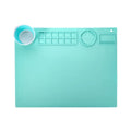 Light blue silicone painting mat with two bowl depressions for water and brushes, placed on a wooden table.