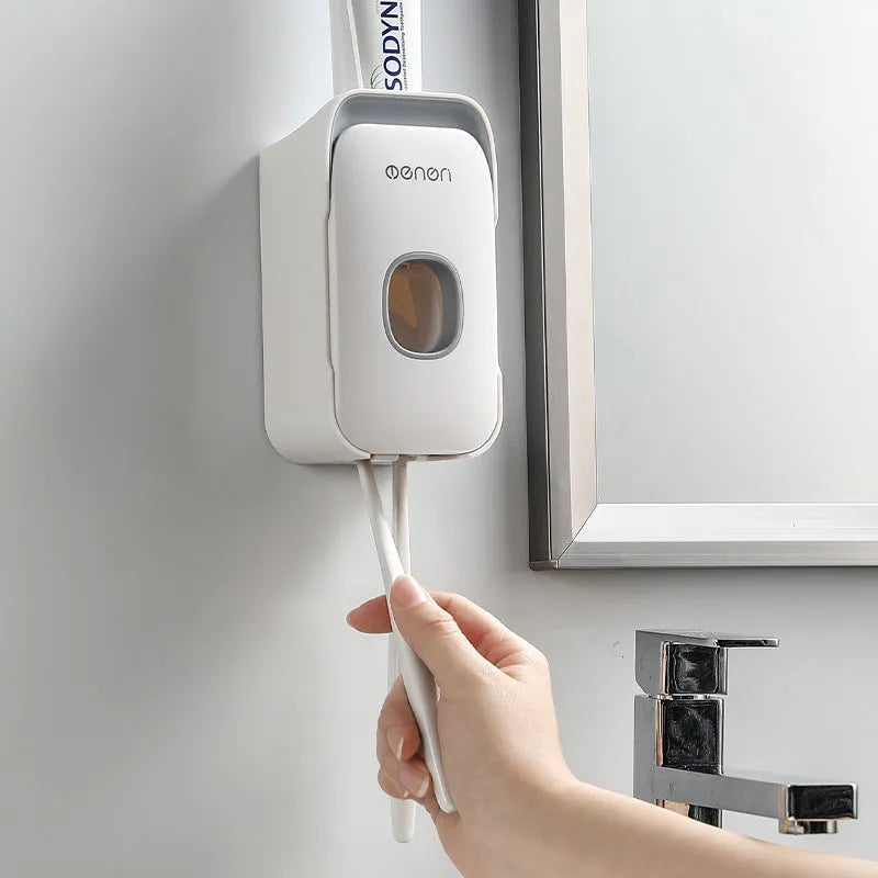 Automatic toothpaste dispenser unit mounted on a wall in a choice of blue, grey, or pink colours.