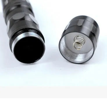 Black aluminium mini LED flashlight on a dark background, shown with AA battery for scale.