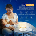 White cylindrical touch-control bedside night light with rechargeable battery on a table.