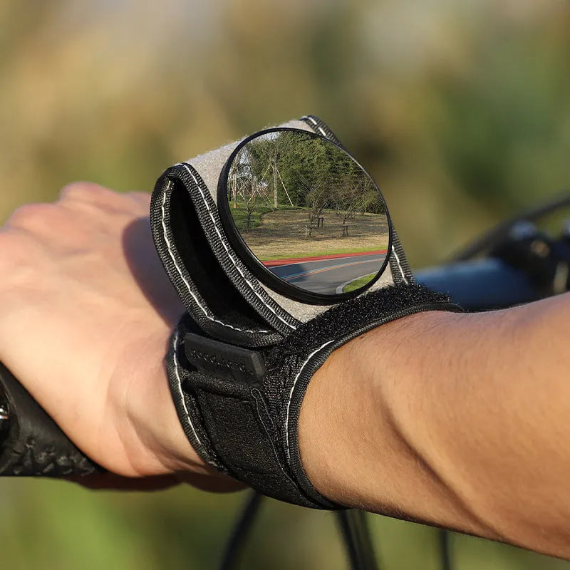 Black bicycle rear-view mirror mounted on an adjustable nylon wrist strap for cycling.